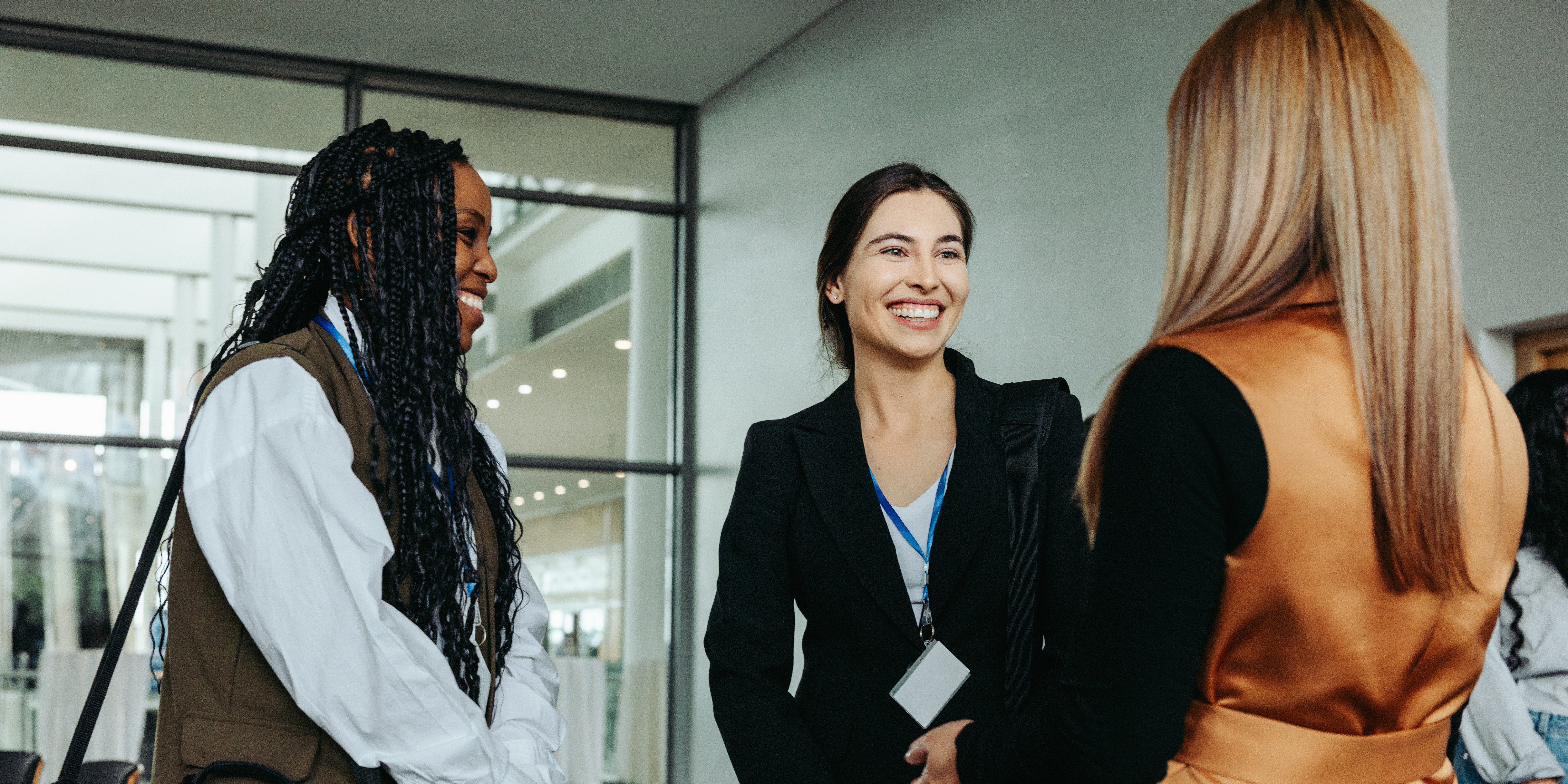 Three nurse leaders wearing conference badges engage in conversation and smile while networking at a professional healthcare conference.