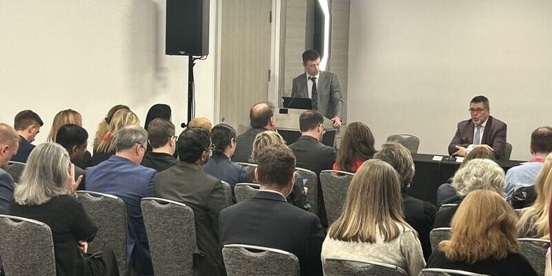 Audience seated in a conference room listening to a speaker presenting at a podium during a healthcare panel session at the Becker’s Annual Meeting.